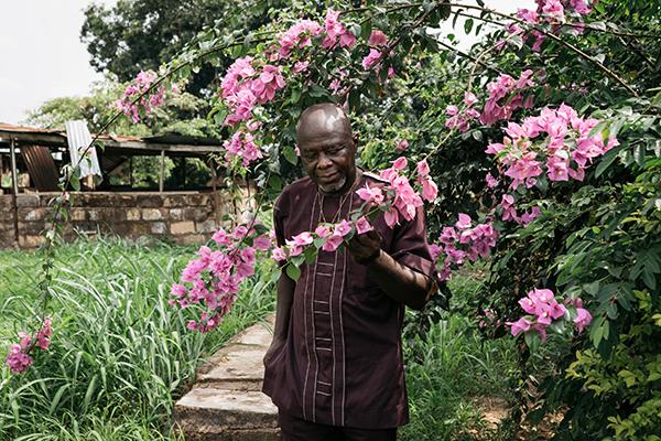 Ike Chime nuuhkii kukkia vanhan kotitalonsa pihalla Enugussa. Kuva: Uwa Iduozee
