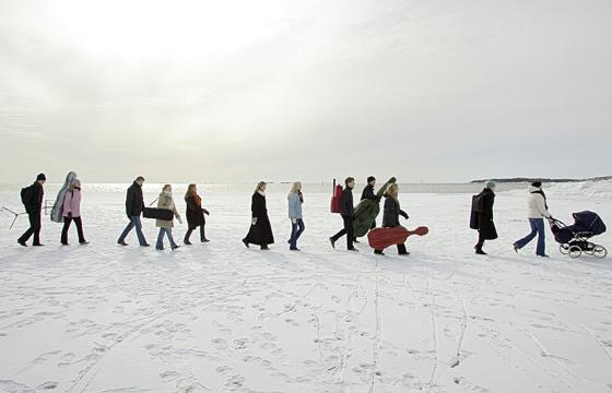 Ihmisiä kävelee jonossa jäällä lumisessa, valkoisessa maisemassa.