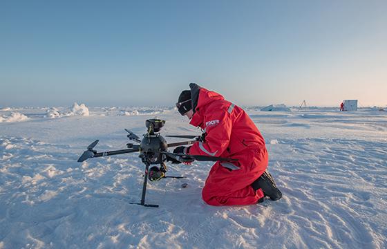 Luminen maisema ja nainen punaisessa haalarissa dronen kanssa.