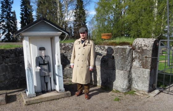 Kirkkohistorioitsija Ville Vauhkonen Ruoveden hautausmaan portilla työskentelevän vaivaisukon kanssa. Vuonna 1993 valmistuneen ukon on veistänyt Marko Salminen, ja se on Ruoveden seurakunnan kolmas vaivaisukko. 