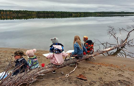Lapsia istumassa puunrungolla järven rannalla.