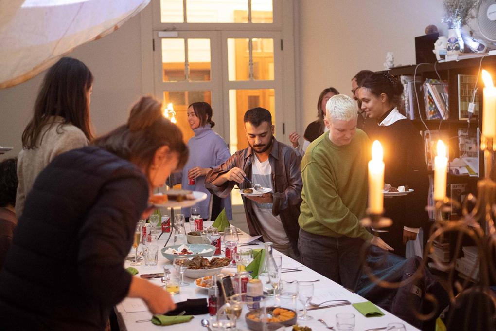 Ihmisiä kokoontuneena ruokapöydän ääreen, etualalla kynttilöitä