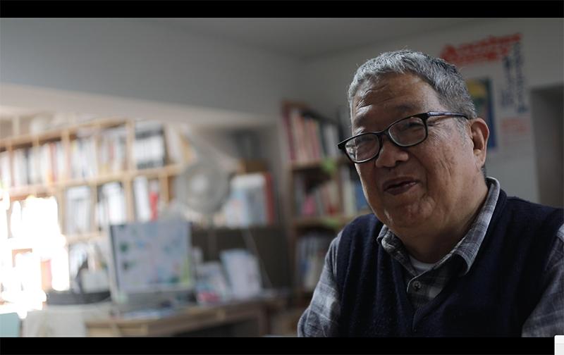 A Japanese man with glasses and grey hair in a library