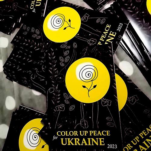 Pöydällä lojuvia mustia värityskirjoja, joiden kannessa kukka keltaisessa pallossa ja teksti Color Up Peace Ukraine.