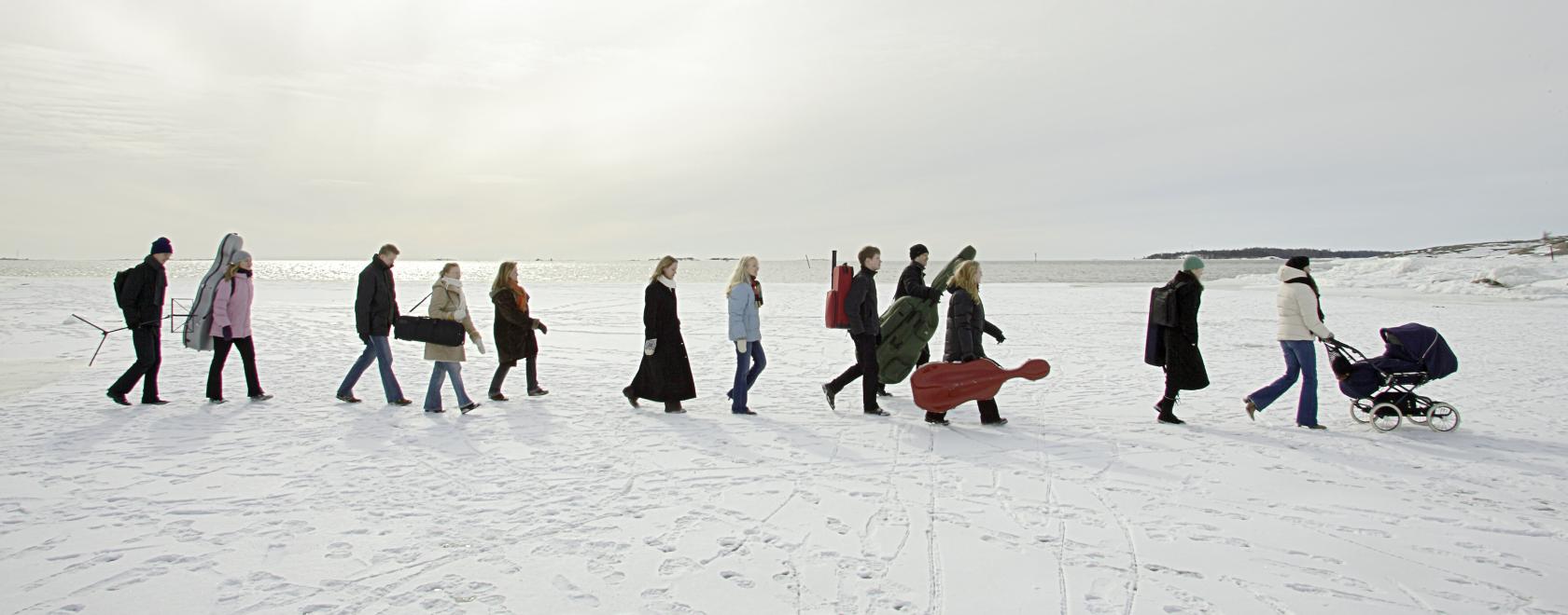 Ihmisiä kävelee jonossa jäällä lumisessa, valkoisessa maisemassa.