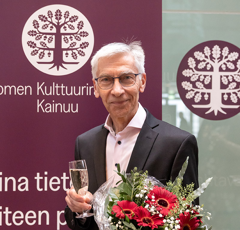 Mies puku päällä kuohuviinilasi ja kukkakimppu kädessään