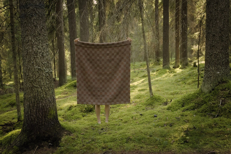 Sammalmetsä, jossa näkyy lakanan takana ihmisen jalat.