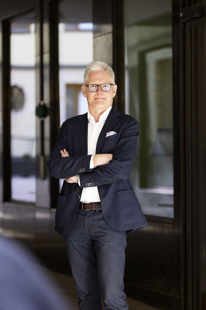 Mies tummassa puvussa seisoo kädet puuskassa