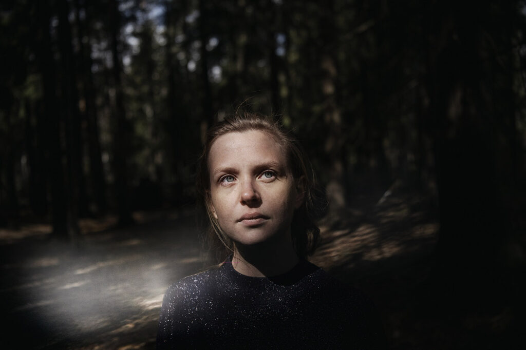 Tummasävyinen kuva naisesta metsässä