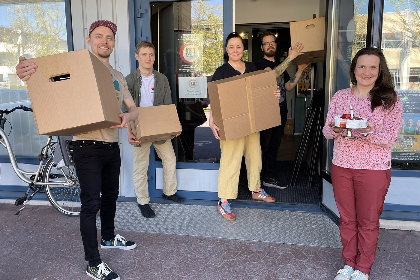 Viisi ihmistä rakennuksen ulkopuolella laatikot käsissään