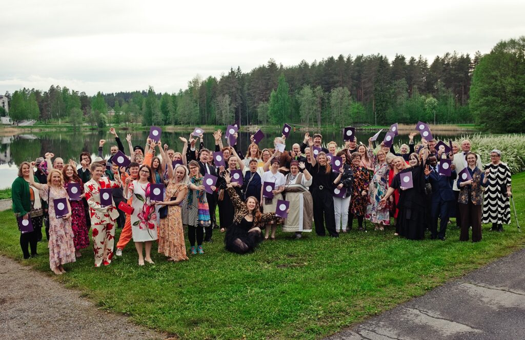 Suuri joukko ihmisiä ulkona nurmikolla juhlavaatteissa