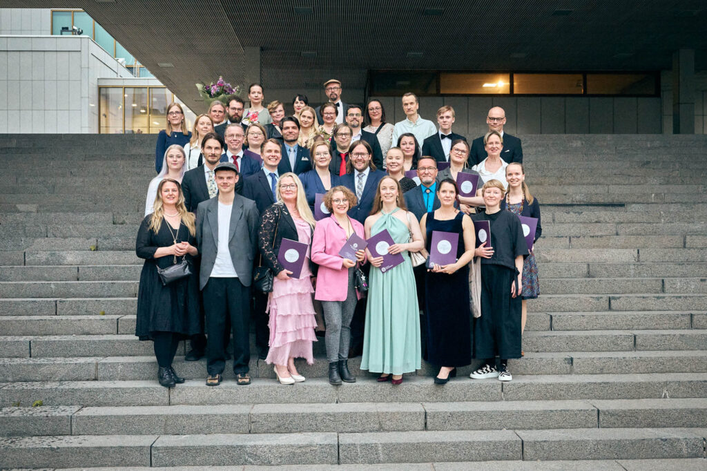 Suuri joukko ihmisiä juhlavaatteissa seisomassa betonirappusilla.