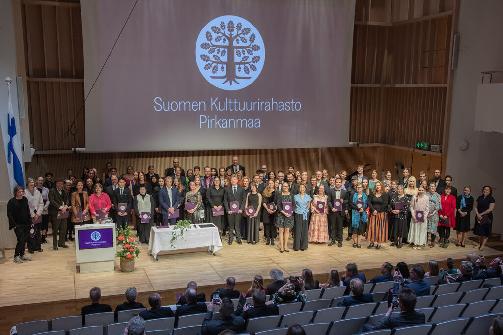 Suuri joukko ihmisiä seisomassa juhlasalin lavalla.