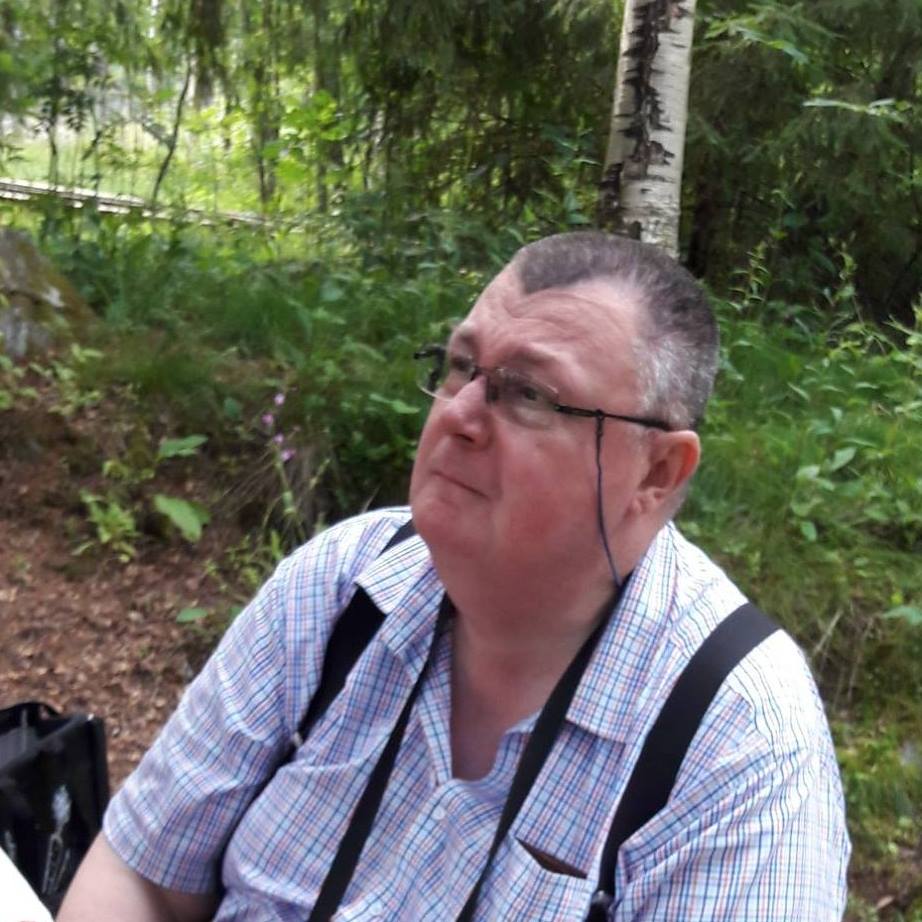 Mies valkoisessa paidassa ja henkseleissä ulkona.