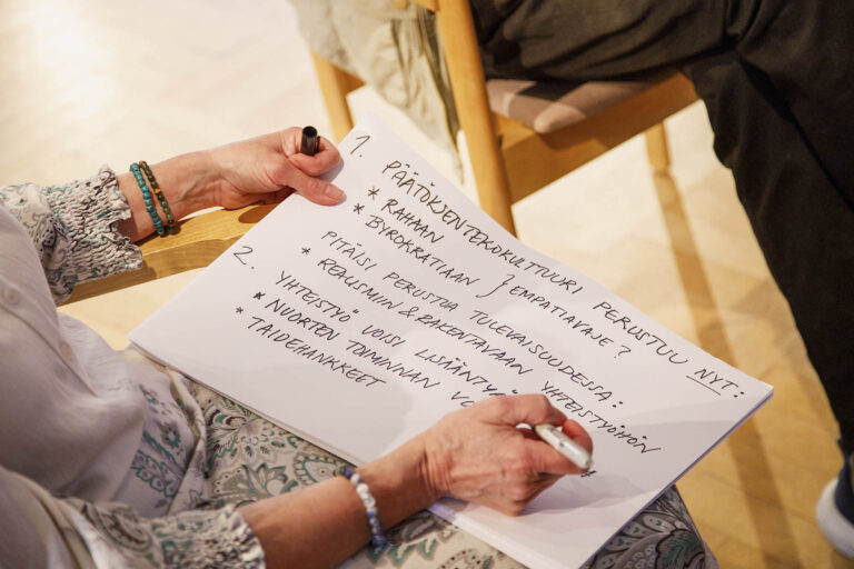 Kirjoitusta sisältävää valkoista paperia pitelevät kädet.