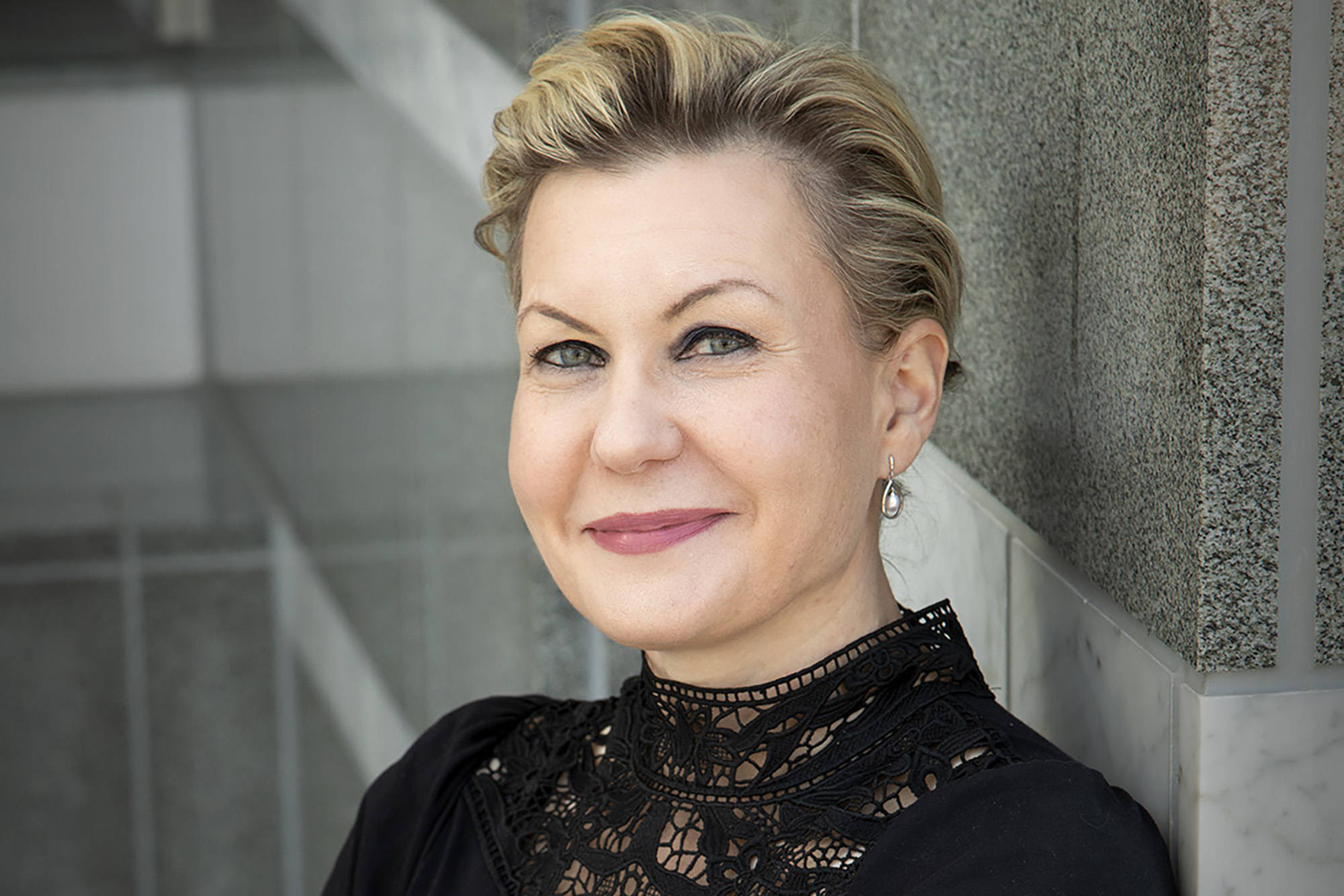 Kasvokuva naisesta, jolla on lyhyet, vaaleat hiukset ja musta pitsipaita