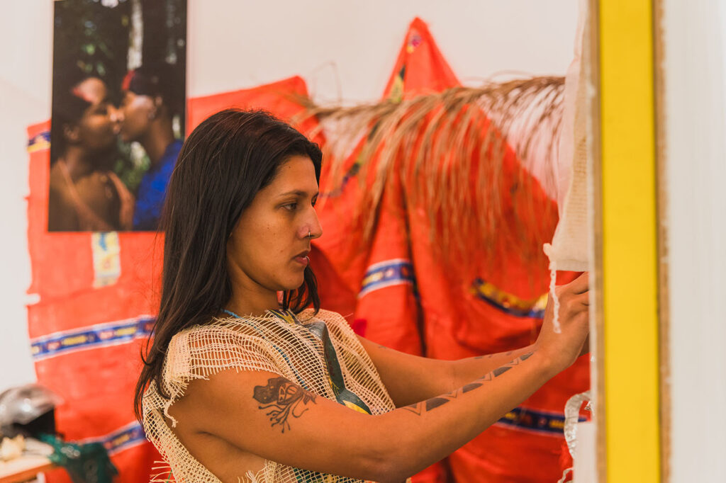 A person with long hair is connecting a paper to a wall. Orange blankets in the backround.