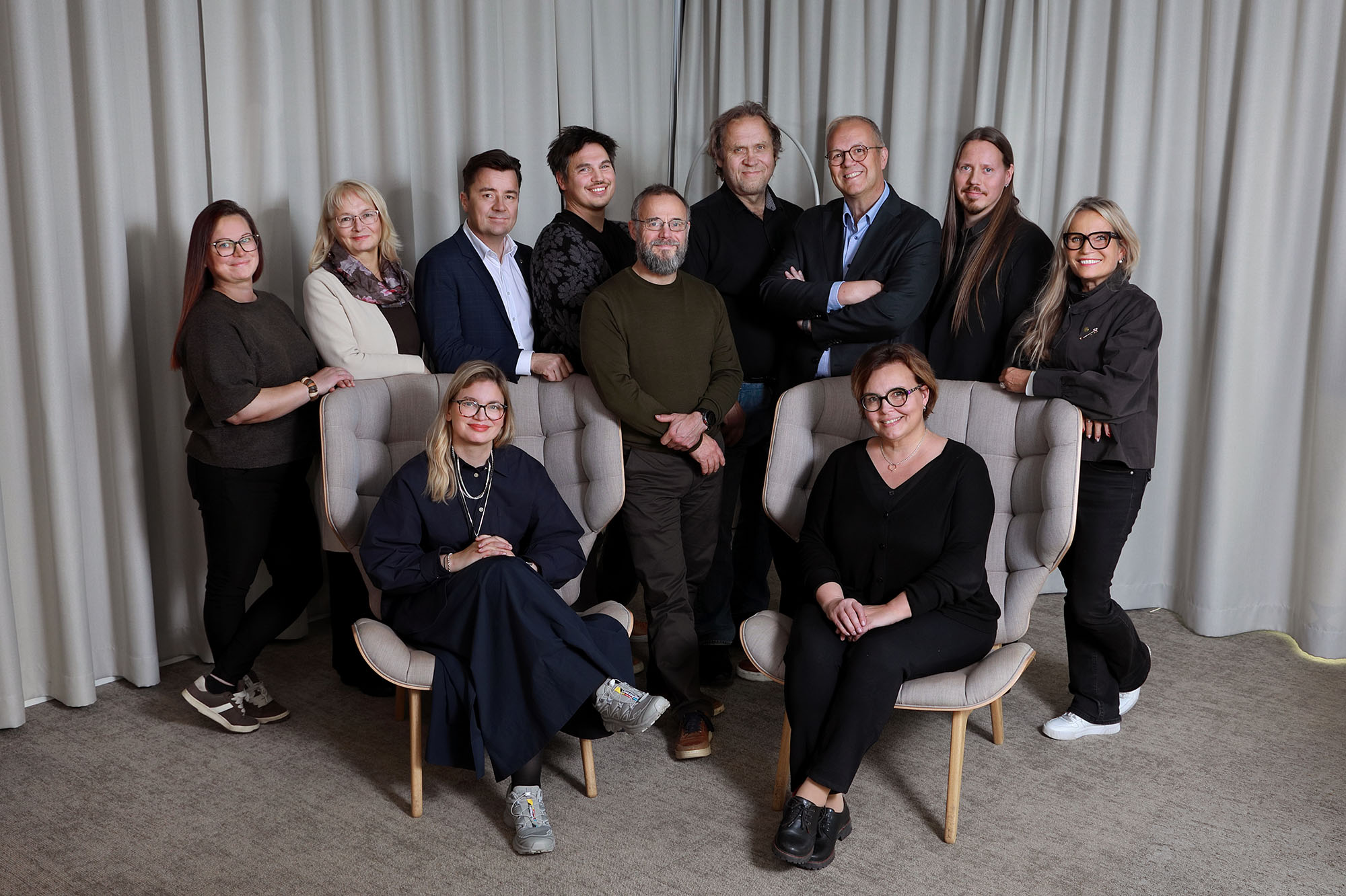 Iso joukko ihmisiä studiossa, taustalla harmaa kangas