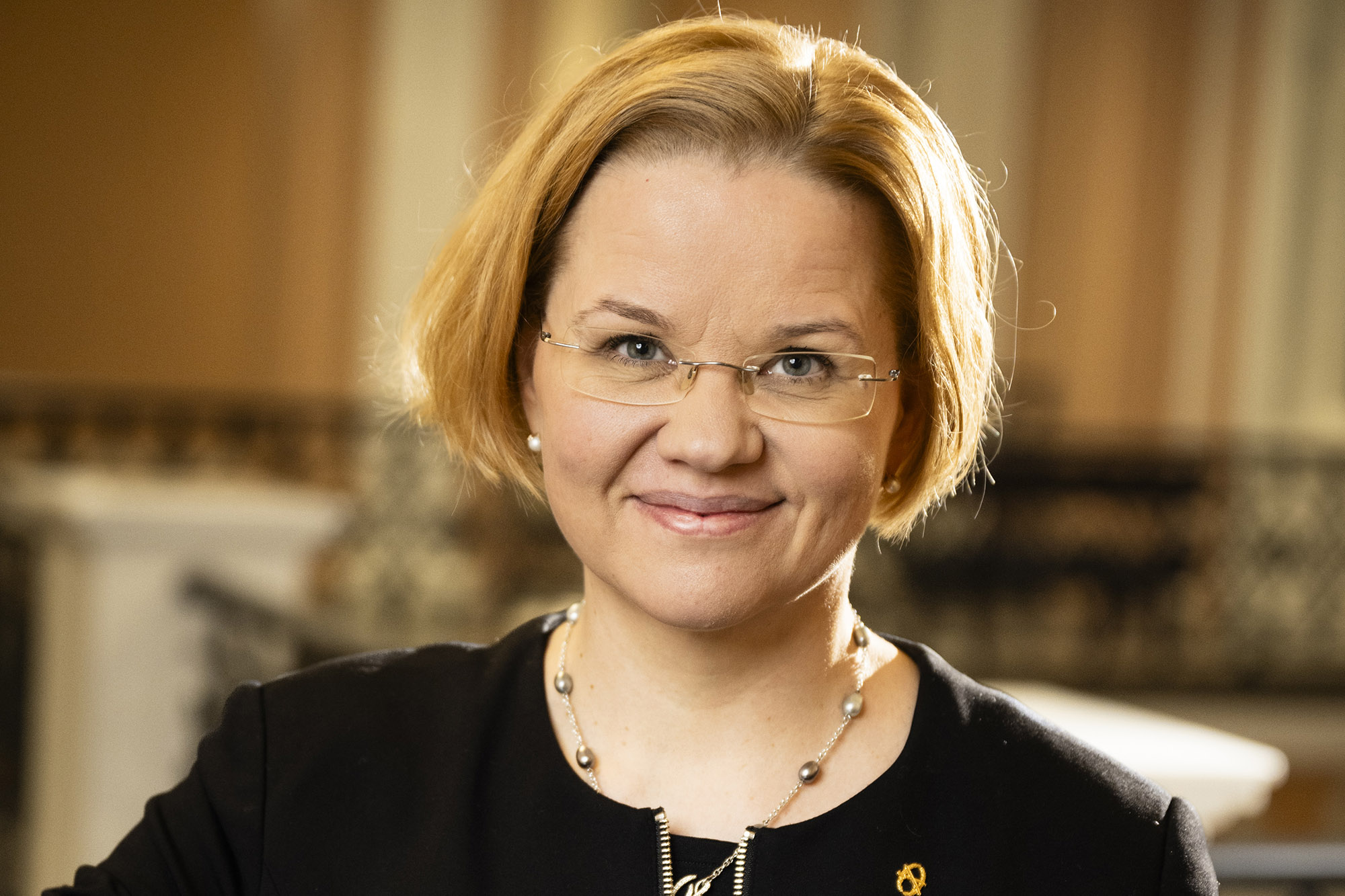 Nainen mustassa jakussa katsoo hymyillen kameraan.